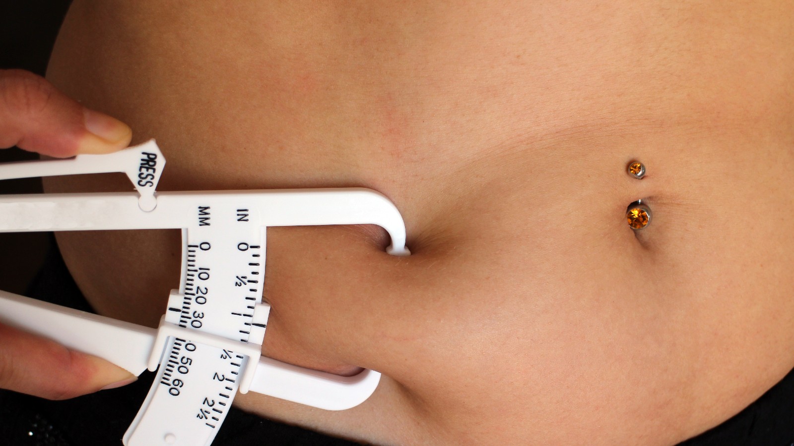 Close-up photo of callipers being used to conduct a skin-fold test of a female abdomen